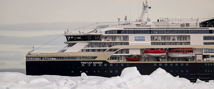 Die MS Fridtjof Nansen von HX Expeditions fährt vor einer eisigen Landschaft durch ruhiges Wasser. Das moderne Hybrid-Expeditionsschiff hebt sich klar von der weißen Kulisse ab.